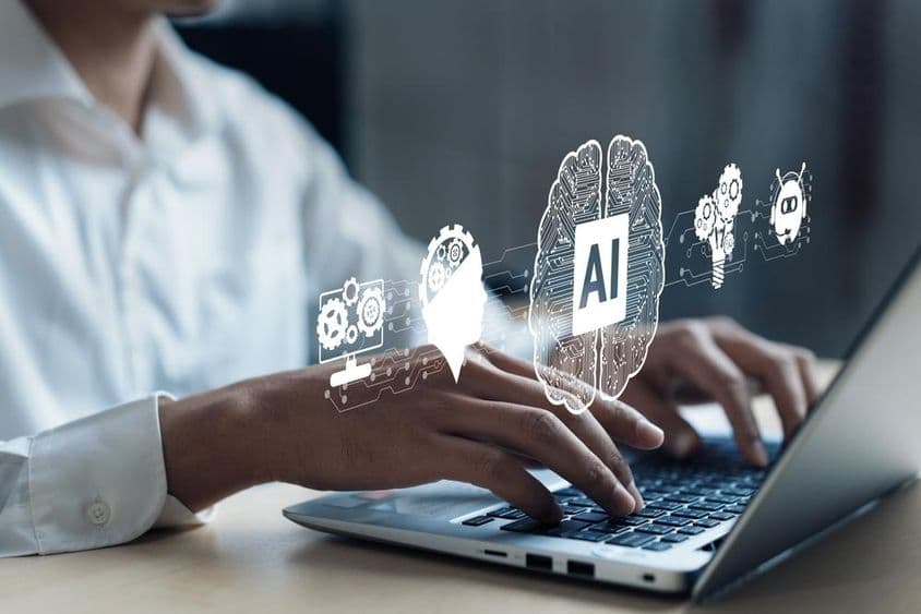 ایک نوٹ بک پر AI دماغ اور دیگر عناصر کی پروجیکشن، انسانی ہاتھ کمپیوٹر پر کام کر رہا ہے۔