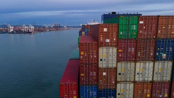 بائیں جانب سمندر کی ایک خلیج دکھائی دے رہی ہے، دائیں جانب دھیرے ہوئے کنٹینرز ہیں۔