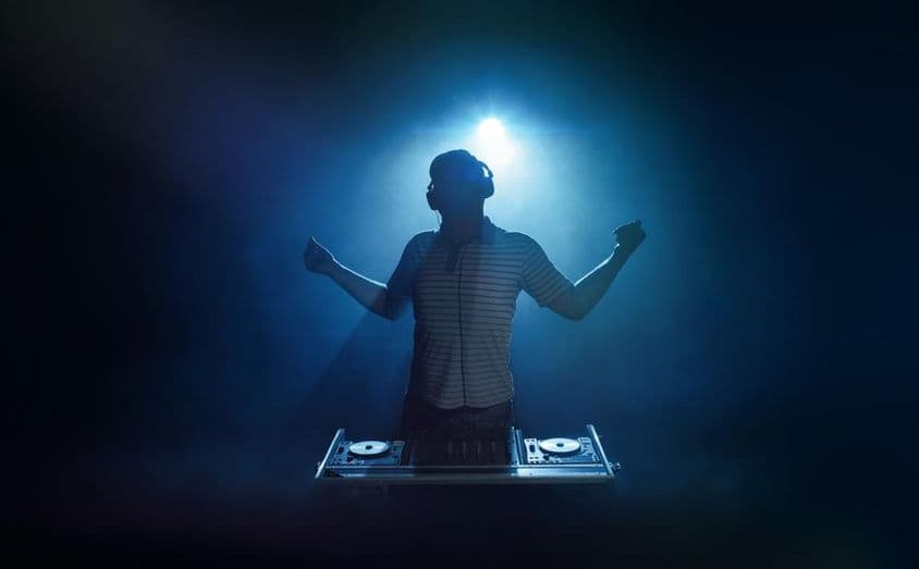 ایک شخص ڈی جے بوتھ کے پیچھے کھڑا ہے۔