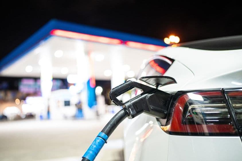 ایک ٹیسلا کو چارج کیا جا رہا ہے، پس منظر میں ایک پیٹرول پمپ دکھائی دے رہا ہے۔