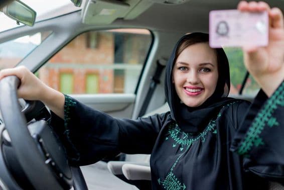 دبئی میں ایک خاتون ایک ہاتھ میں ڈرائیورز لائسنس اور دوسرے ہاتھ سے اسٹئرنگ ویل تھامے مسکراتی ہیں۔