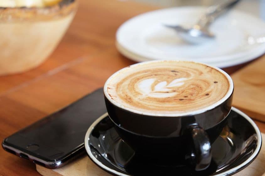 کپ کے ساتھ میز پر پڑا ہوا ایک فون کے پاس کیپوچینو