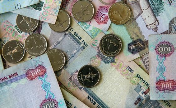 دبئی کاغذی کرنسی میز پر بکھری ہوئی اور اوپر 1 درہم کے سکے رکھے ہوئے۔