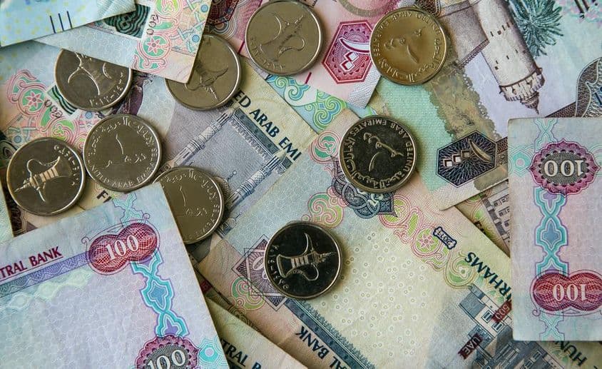 دبئی کاغذی کرنسی میز پر بکھری ہوئی اور اوپر 1 درہم کے سکے رکھے ہوئے۔