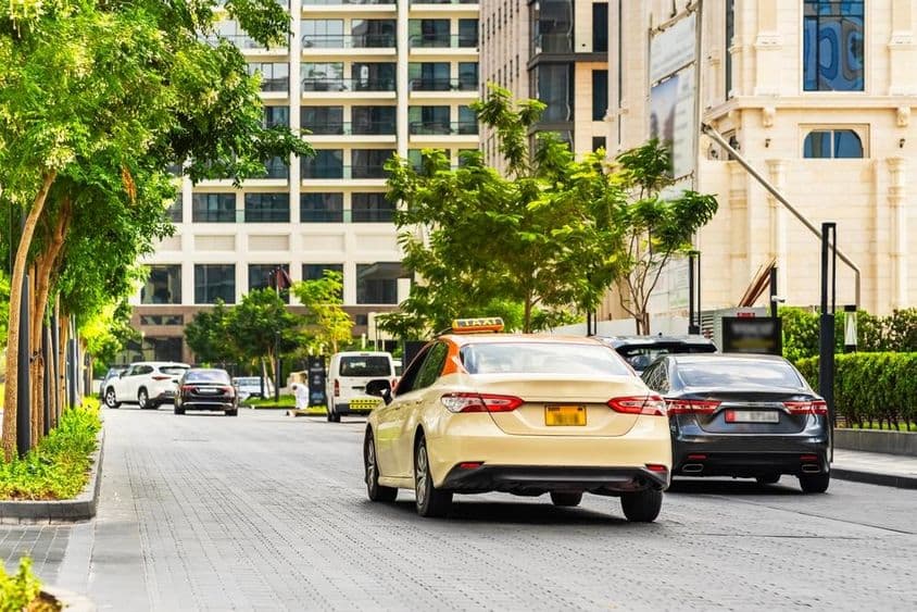 دبئی کی سڑک پر گاڑیاں، سامنے میں ایک ٹیکسی اور پس منظر میں مکانات۔