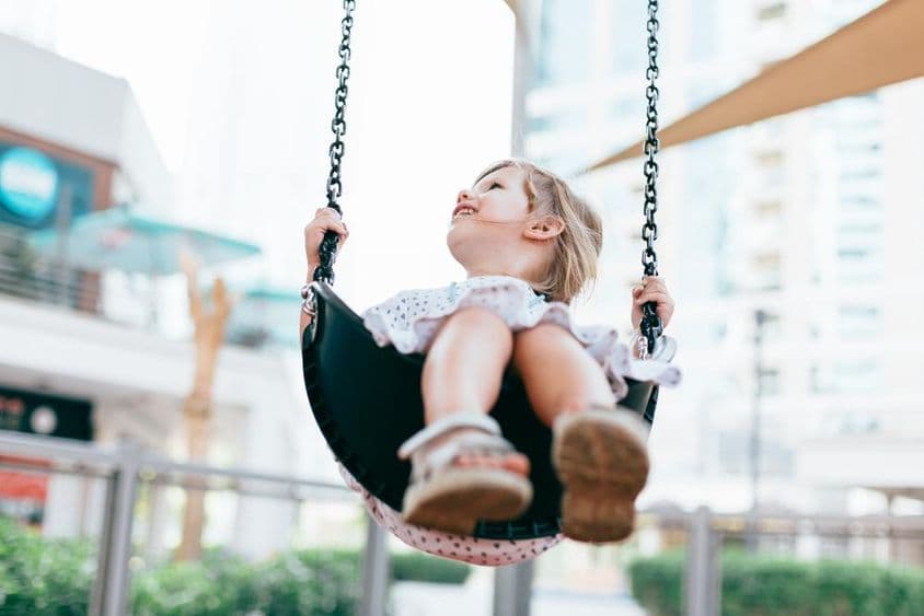 خوشحال چھوٹی بچی کنڈرگارٹن کے صحن میں جھولا جھول رہی ہے۔