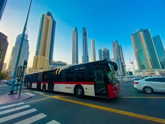 دبئی بس جس کے پس منظر میں فلک بوس عمارتیں ہیں۔