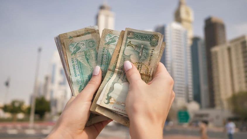 دبئی کی اسکائی سکریپرز کے پس منظر میں UAE کرنسی پکڑے ہوئی ایک لڑکی۔