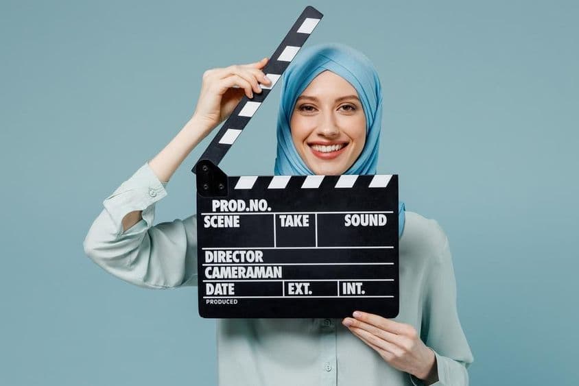 عبایا حجاب میں نوجوان عرب مسلم خاتون کلاسک بلیک فلم کلپر پکڑے ہوئے