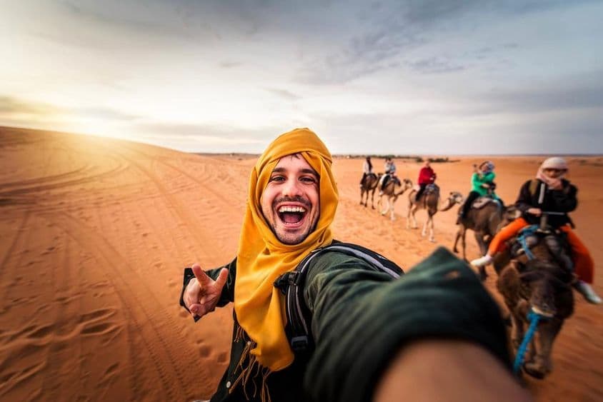 خوش سیاح صحراء میں اونٹ کی سواری کا لطف اٹھاتا ہوا۔