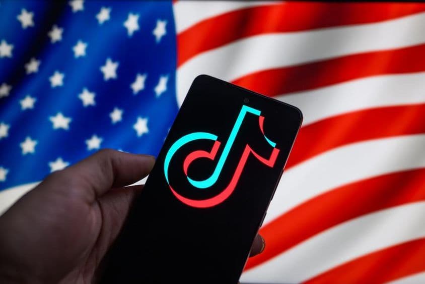 اسمارٹ فون پر TikTok علامت جبکہ پس منظر میں امریکی جھنڈا دکھایا گیا ہے۔