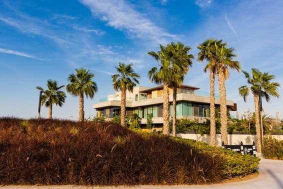 دبئی، ولا جو کھجور کے درختوں کے بیچ میں ہے اور بادلوں والی سورج غروب کا منظر پیش کرتا ہوا