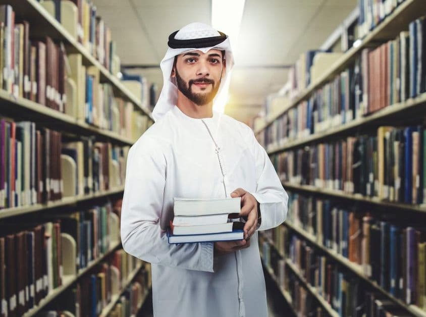 عربی طالب علم کتب لائبریری میں پکڑے کھڑا ہے۔