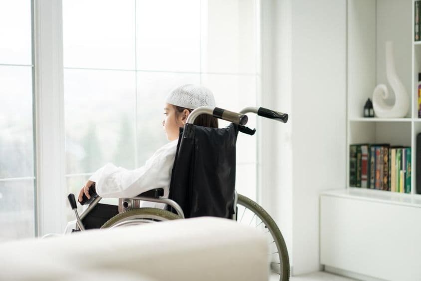 ایک جوان لڑکا وہیل چیئر میں بیٹھا ہوا کھڑکی سے باہر دیکھ رہا ہے۔