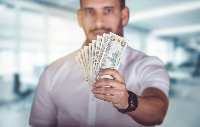 آدمی ہاتھ میں متحدہ عرب امارات کے درہم کی نقدی پکڑے ہوئے۔