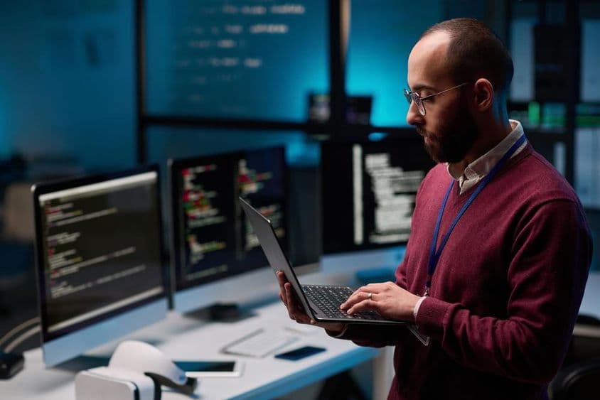 آئی ٹی اور سائبر سیکیورٹی دفتر میں ایک کھلے لیپ ٹاپ کو پکڑے ہوئے کمپیوٹر پروگرامر۔