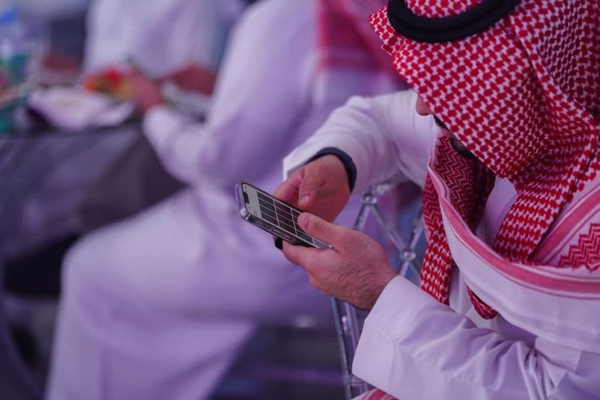 عرب آدمی موبائل فون پر کام کر رہا ہے، پیغام پڑھ یا لکھ رہا ہے۔