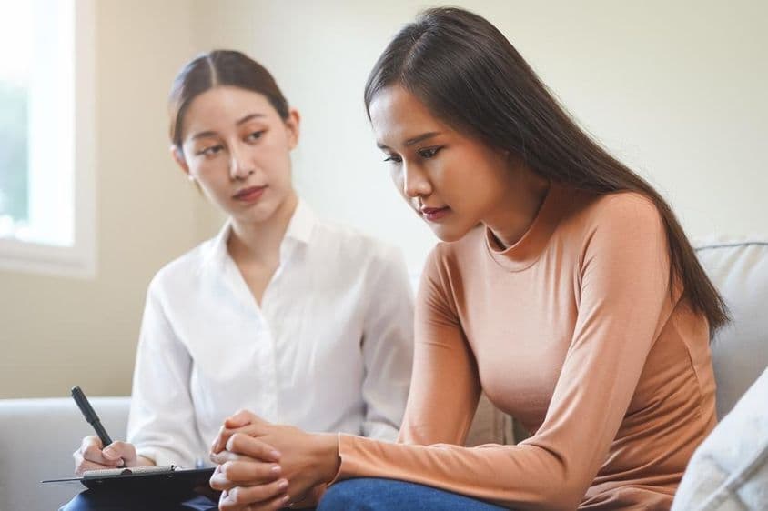 اداس ایشیائی نوجوان خاتون ماہر نفسیات سے مشورہ کر رہی ہے۔