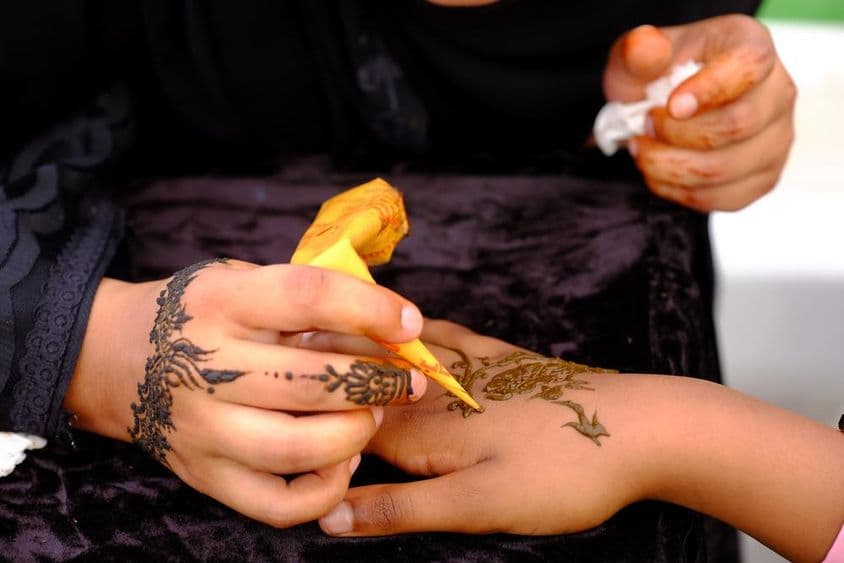 ایک لڑکی دوسری کی ہتھیلی پر مہندی کا ڈیزائن لگا رہی ہے۔