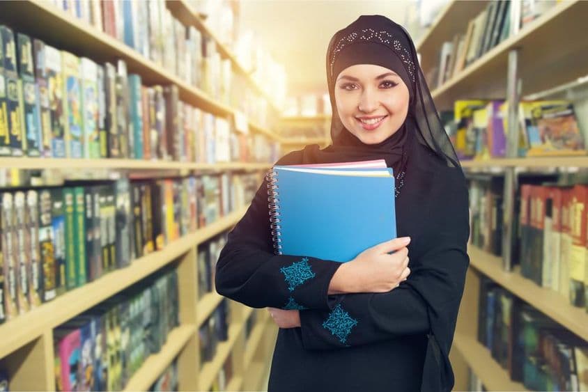کتب کے ساتھ لائبریری میں کھڑا عرب طالب علم