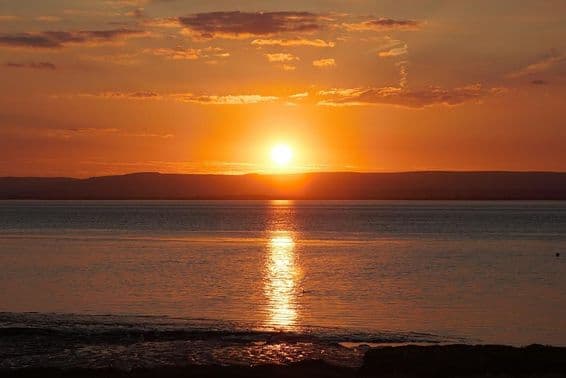 گرمی کے خطرناک مقام کے دوران پانی اور بادلوں پر غروب آفتاب کا عکس۔