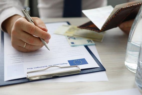 ایک شخص پاسپورٹ تھامے اور شینجن ویزا کی درخواست پر ذاتی معلومات درج کرتا ہوا۔