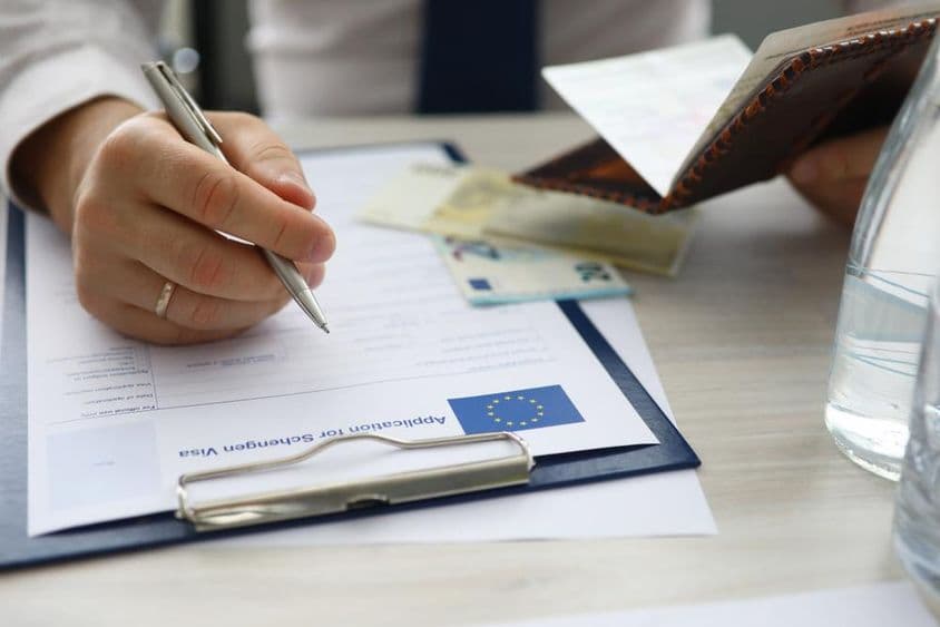 ایک شخص پاسپورٹ تھامے اور شینجن ویزا کی درخواست پر ذاتی معلومات درج کرتا ہوا۔