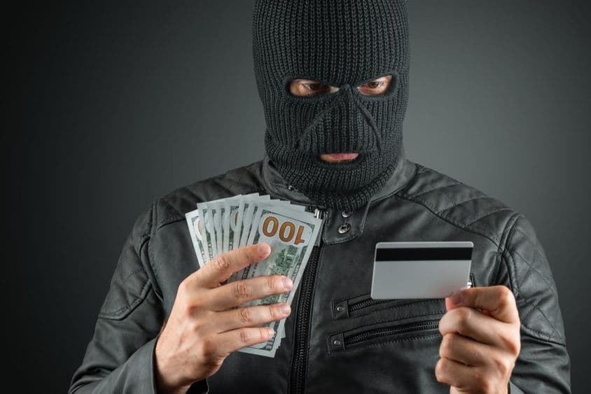 مجرم اسکی ماسک میں سیاہ پس منظر کے خلاف کریڈٹ کارڈ پکڑے ہوئے۔