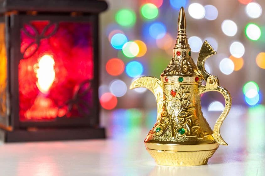 عرب کافی کا برتن اور لیمپ جس کے پس منظر میں رنگ برنگی، دھندلی روشنیاں ہیں۔