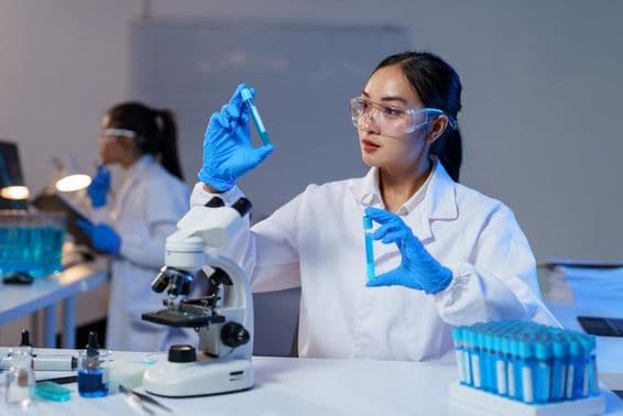 لیب کوٹ اور دستانے میں ایشیائی خاتون سائنسدان دو ٹیسٹ ٹیوبز کا موازنہ کرتے ہوئے