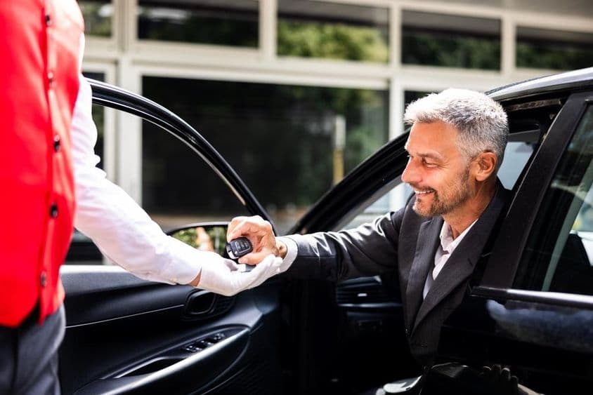 کاروباری شخص ہوٹل کی پارکنگ میں کار کی چابیاں ویلٹ کو دیتا ہوا