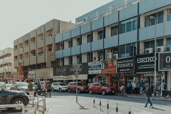 دبئی کے بر دبئی میں ایک مصروف سڑک، زیورات کی دکانیں، پیدل چلنے والے اور دھوپ کے دن گاڑیاں