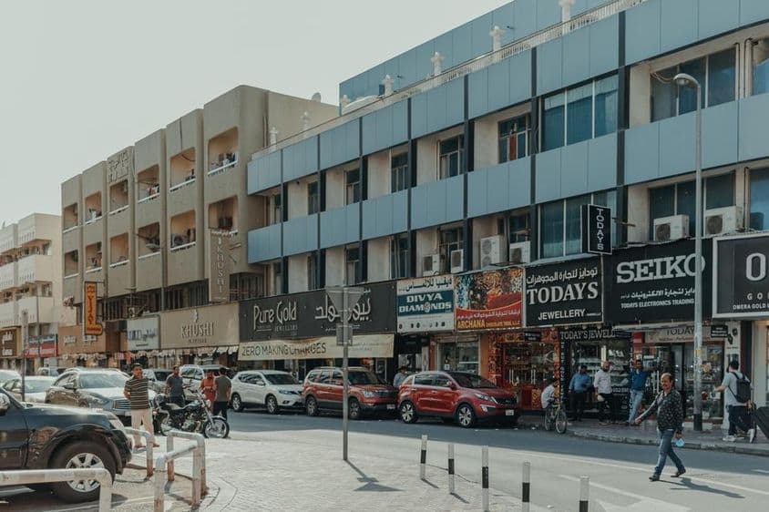 دبئی کے بر دبئی میں ایک مصروف سڑک، زیورات کی دکانیں، پیدل چلنے والے اور دھوپ کے دن گاڑیاں