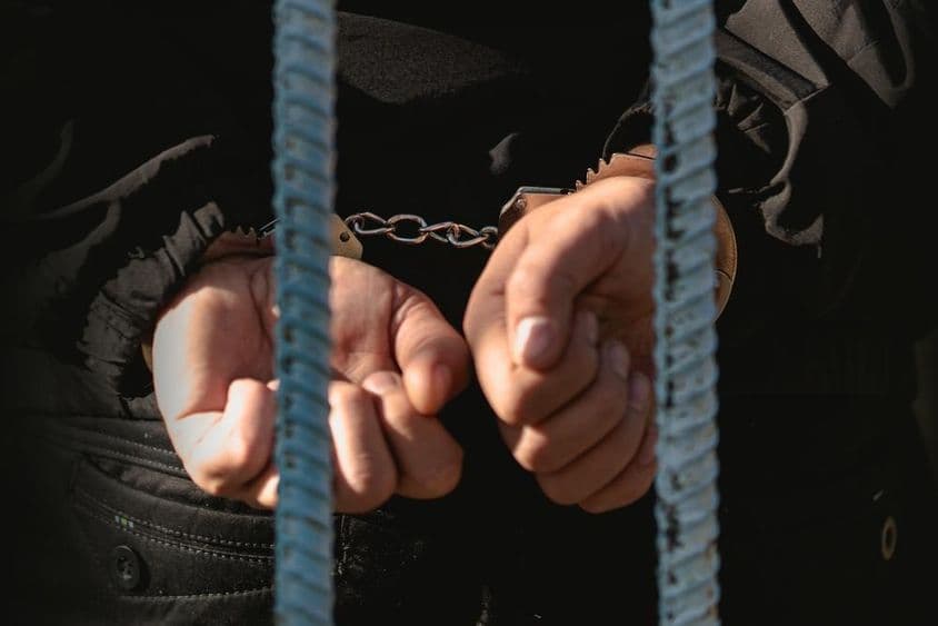 پولیس سٹیشن میں سلاخوں کے پیچھے ہتھکڑیوں میں بندھا ہوا آدمی۔