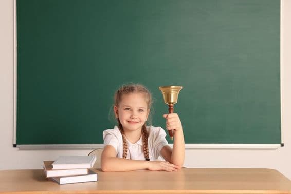 کلاس روم میں اسکول کی گھڑی کے ساتھ میز پر بیٹھا طالب علم۔