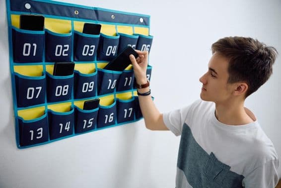 طالب علم اسمارٹ فون کو دیوار پر لگے فون آرگنائزر میں چھوڑ رہا ہے۔