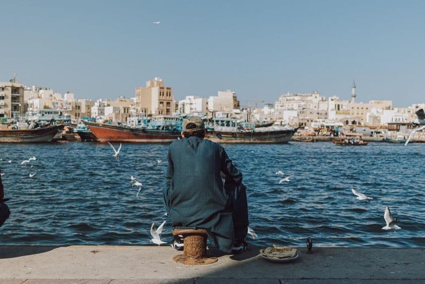 دبئی کریک میں کشتیاں اور گلیوں کے ساتھ پانی کا منظر دیکھتے ہوئے ایک شخص