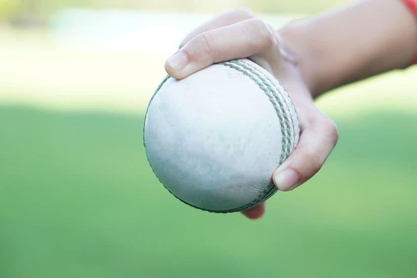 ایک کرکٹر سفید چمڑے کی کرکٹ بال کو تھامے ہوئے۔