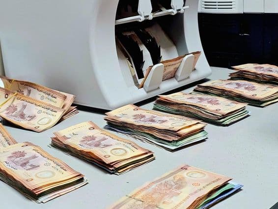 کرنسی گننے والی مشین کے ساتھ میز پر اماراتی Dirham نوٹوں کی صف بدہ چیزیں موجود ہیں۔