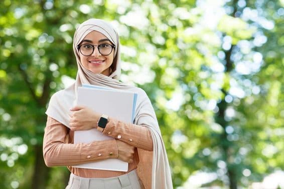 اسکول کو واپسی، عرب خاتون حجاب اور عینک میں کتابیں پکڑے پارک میں۔