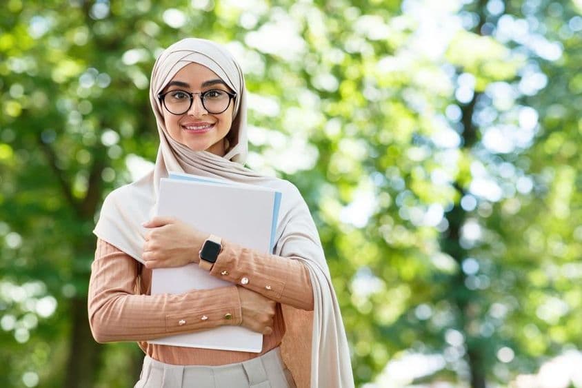 اسکول کو واپسی، عرب خاتون حجاب اور عینک میں کتابیں پکڑے پارک میں۔