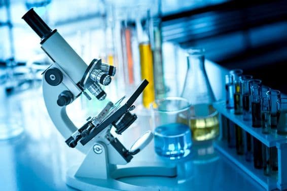 میز پر ایک خوردبین جس کے ساتھ کیمیائی نلیاں اور شیشگر