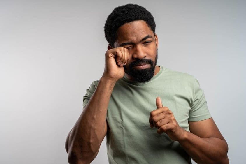 ایک شخص جو اپنی آنکھیں بے چینی سے رگڑ رہا ہے، جسے جلن اور تھکاوٹ محسوس ہو رہی ہے۔