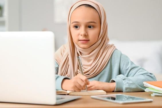 چھوٹی مسلم لڑکی حجاب پہنے گھر پر ہوم ورک کر رہی ہے۔